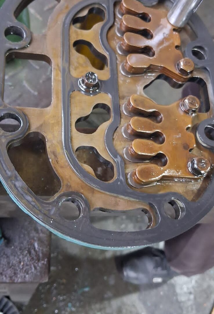 Compressor valve plate with suction and discharge reed valves being serviced in the workshop