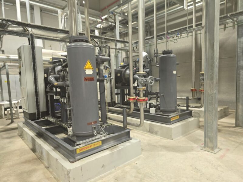 Industrial refrigeration plant room with screw compressor packages on isolated plinths and vertical liquid receivers