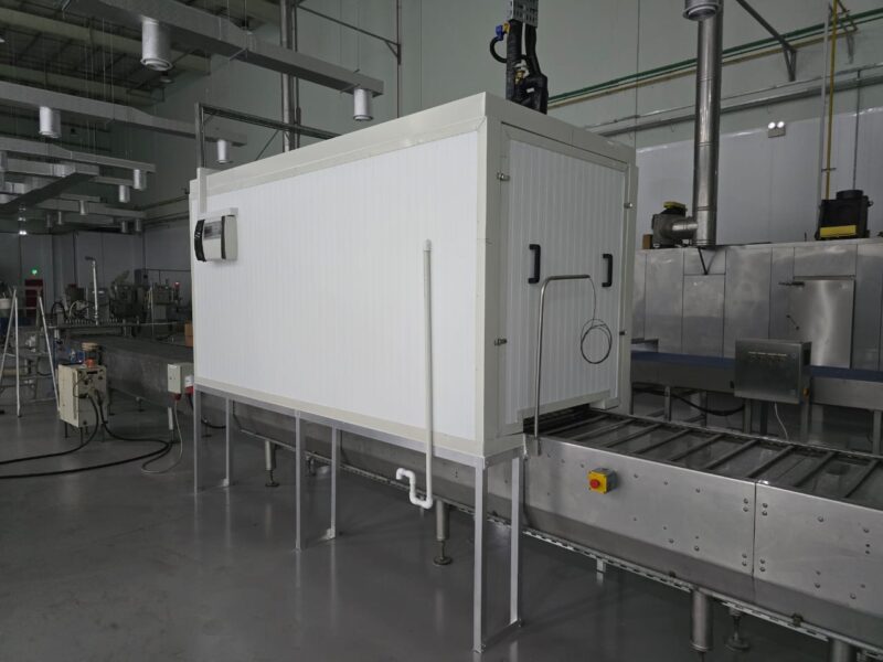Insulated inline cooling tunnel installed over a stainless steel conveyor in a food production facility