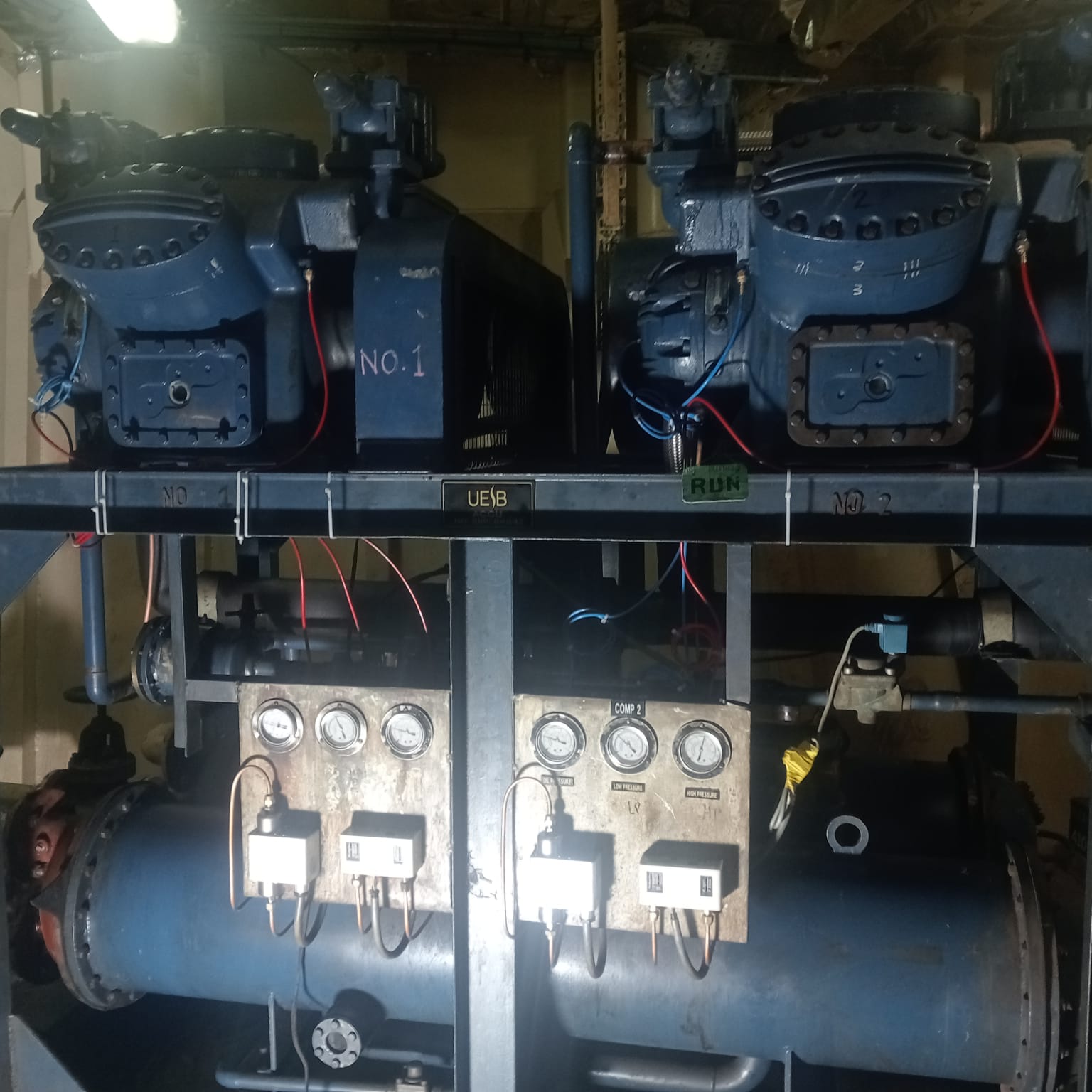 Twin marine refrigeration compressors mounted on a common receiver skid in a vessel engine room, with suction and discharge pressure gauges